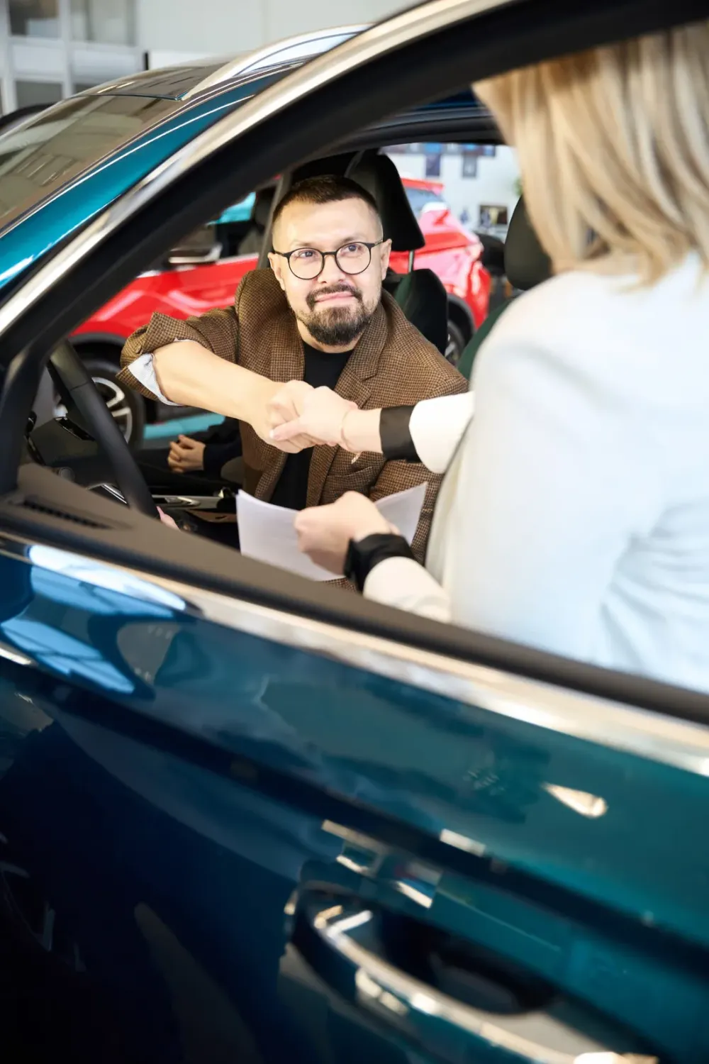 Car buyer in the driver's seat shaking hands with a salesperson